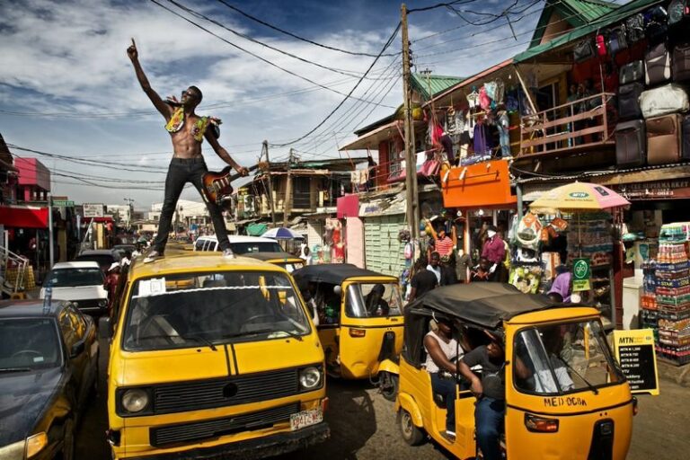 Man standing on a yellow danfo bus in a busy market in Lagos